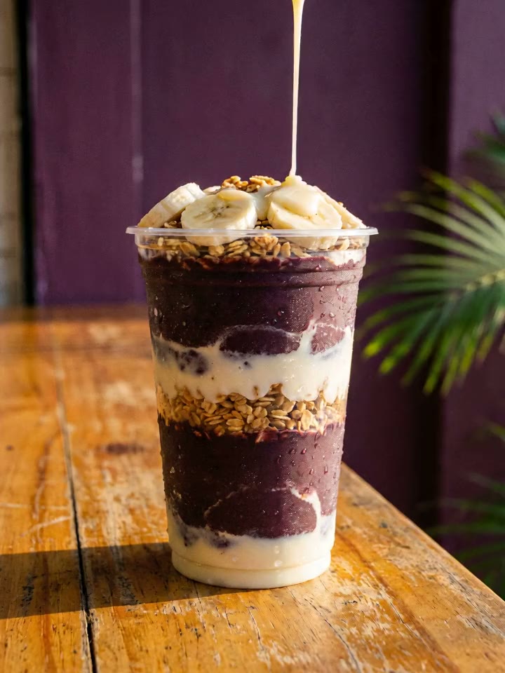 Copo de açaí em camadas com creme e granola, banana por cima